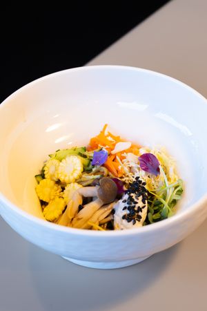 Elegant bowl of mixed vegetables and grains garnished with purple flowers and black sesame seeds.
