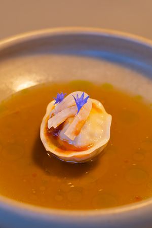 Scallops with blue edible flowers floating in a golden consommé broth.