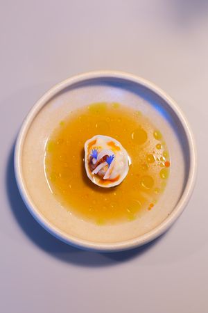 Elegant seafood dish with blue flowers in a golden broth served in white ceramic bowl.