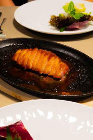 Sliced glazed duck breast served with dark sauce on cast iron plate alongside fresh greens.