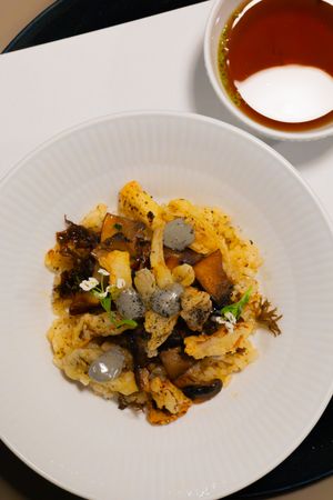 Roasted cauliflower and mushrooms garnished with herbs on a white plate served with dipping sauce.