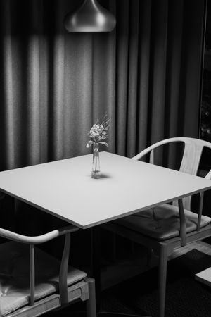 Minimalist black and white dining setup with single flower vase on white table.