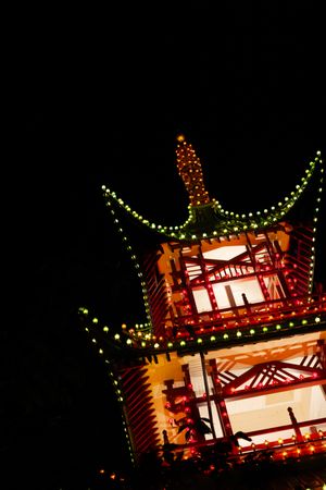 Illuminated traditional Asian pagoda tower decorated with glowing orange lights against dark night sky.