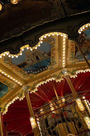 Ornate carousel ceiling with mirrors, lights and red canopy details in classic amusement park style.