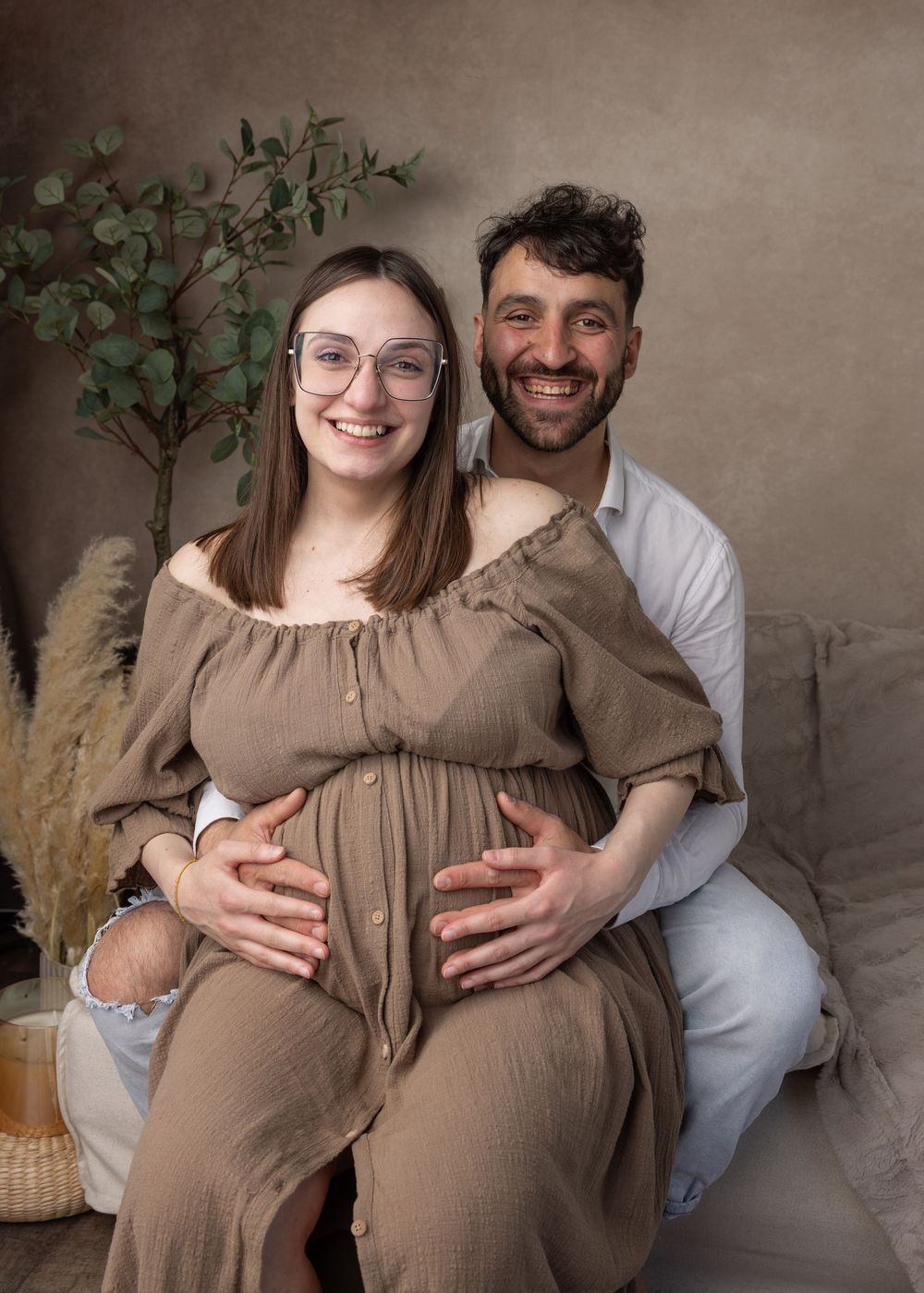 A couple poses together for maternity photos against a neutral backdrop, showing the progression of their pregnancy journey.