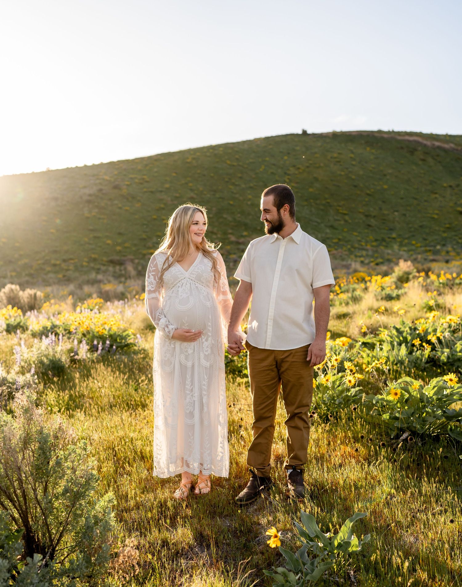 A maternity photo session among wildflowers on a hillside at sunset.