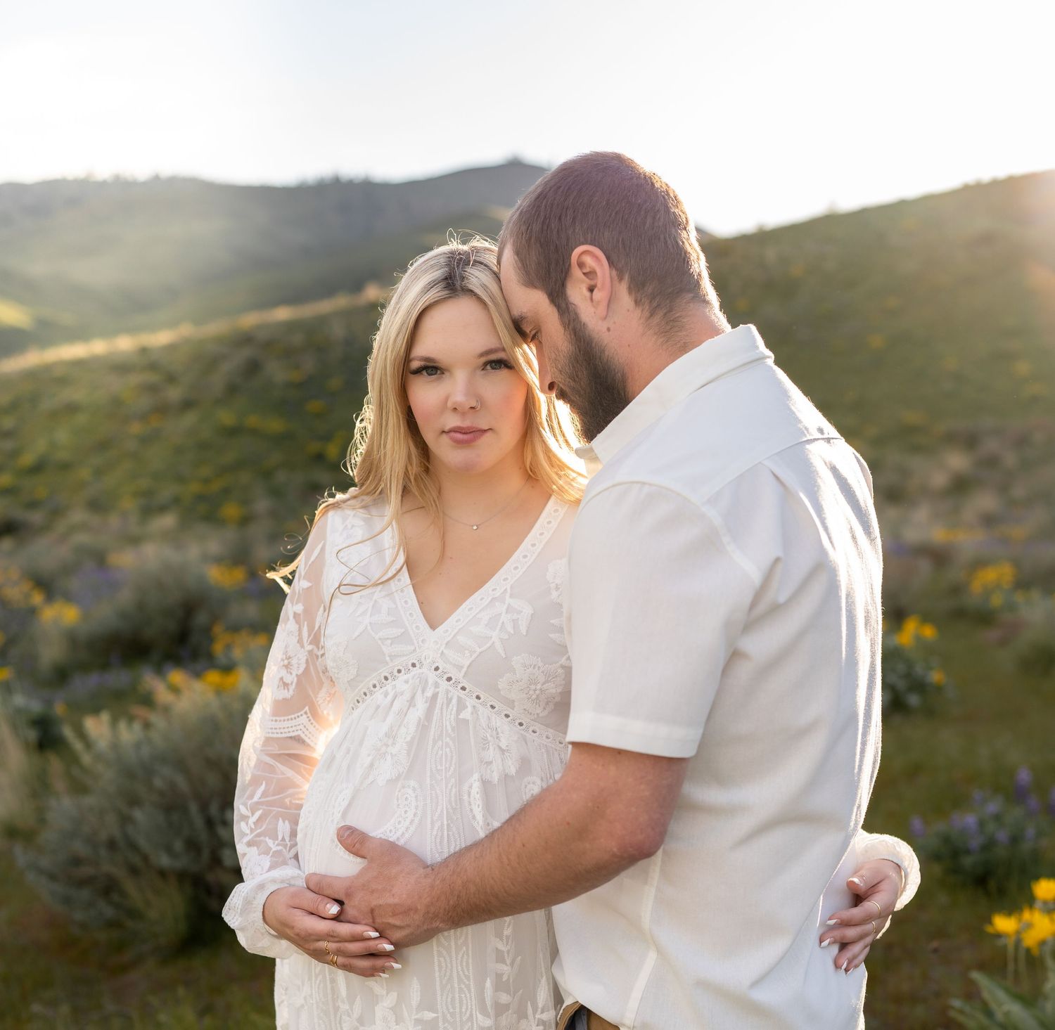 A tender maternity moment captured against rolling hills at golden hour.