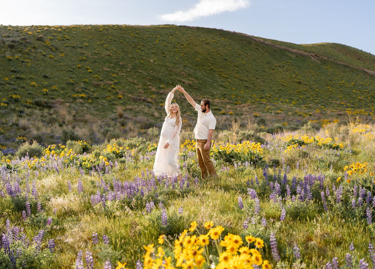 A romantic couple dances together in a meadow filled with yellow wildflowers and purple lupines.