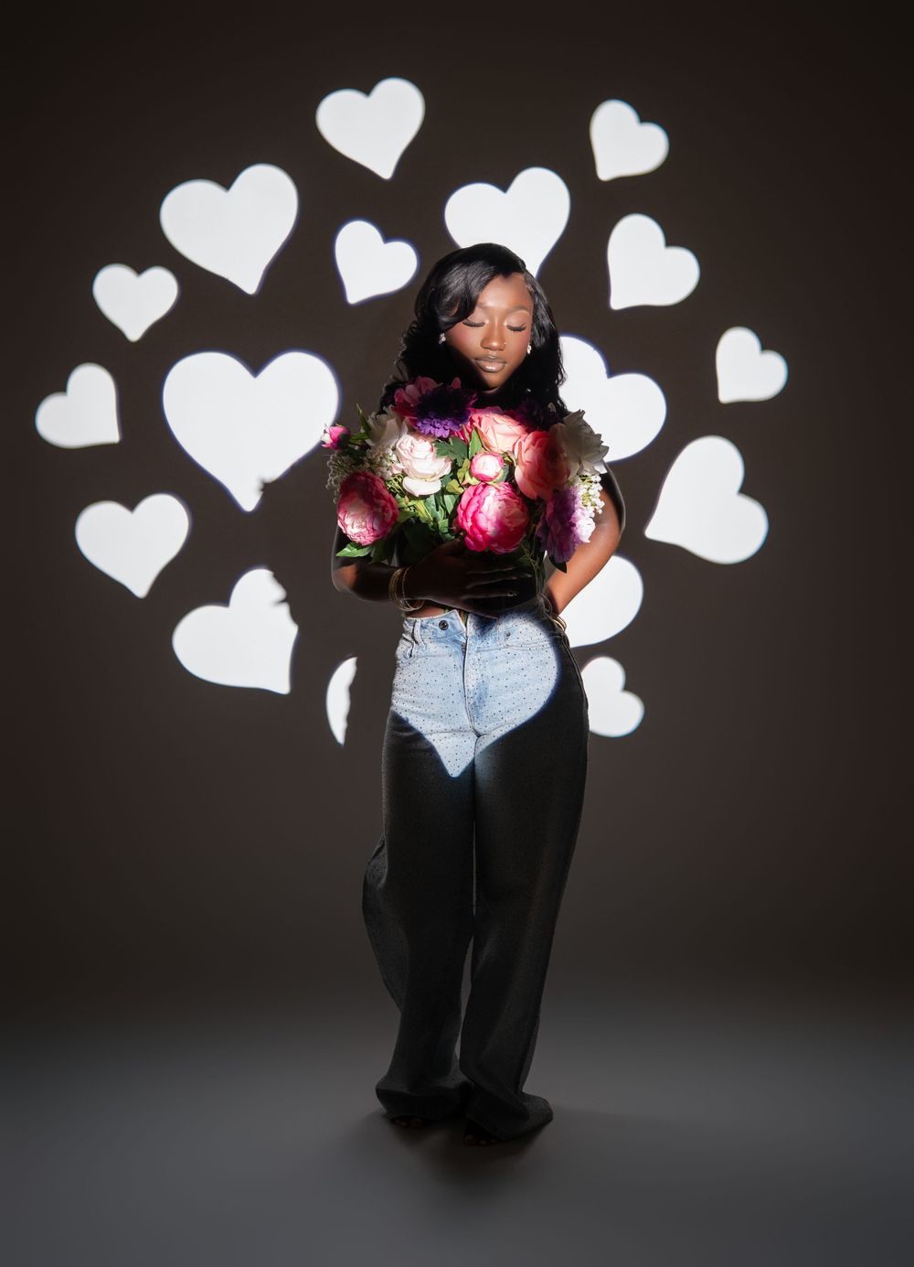 A romantic portrait against dark background with white heart graphics and a bouquet of pink and white flowers.