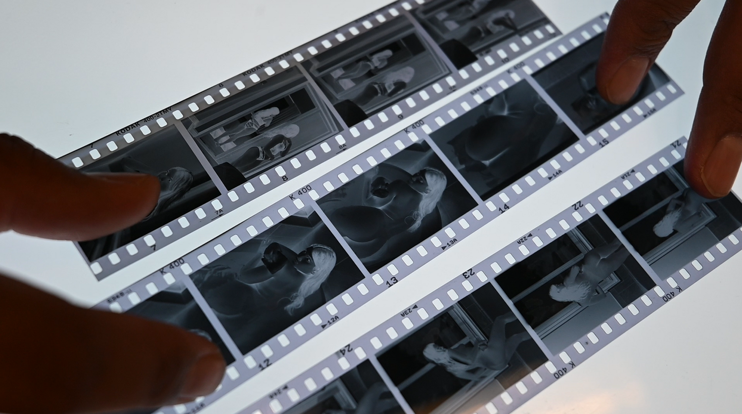 Someone's fingers shown holding developed black and white photo negatives in strips against a white background.