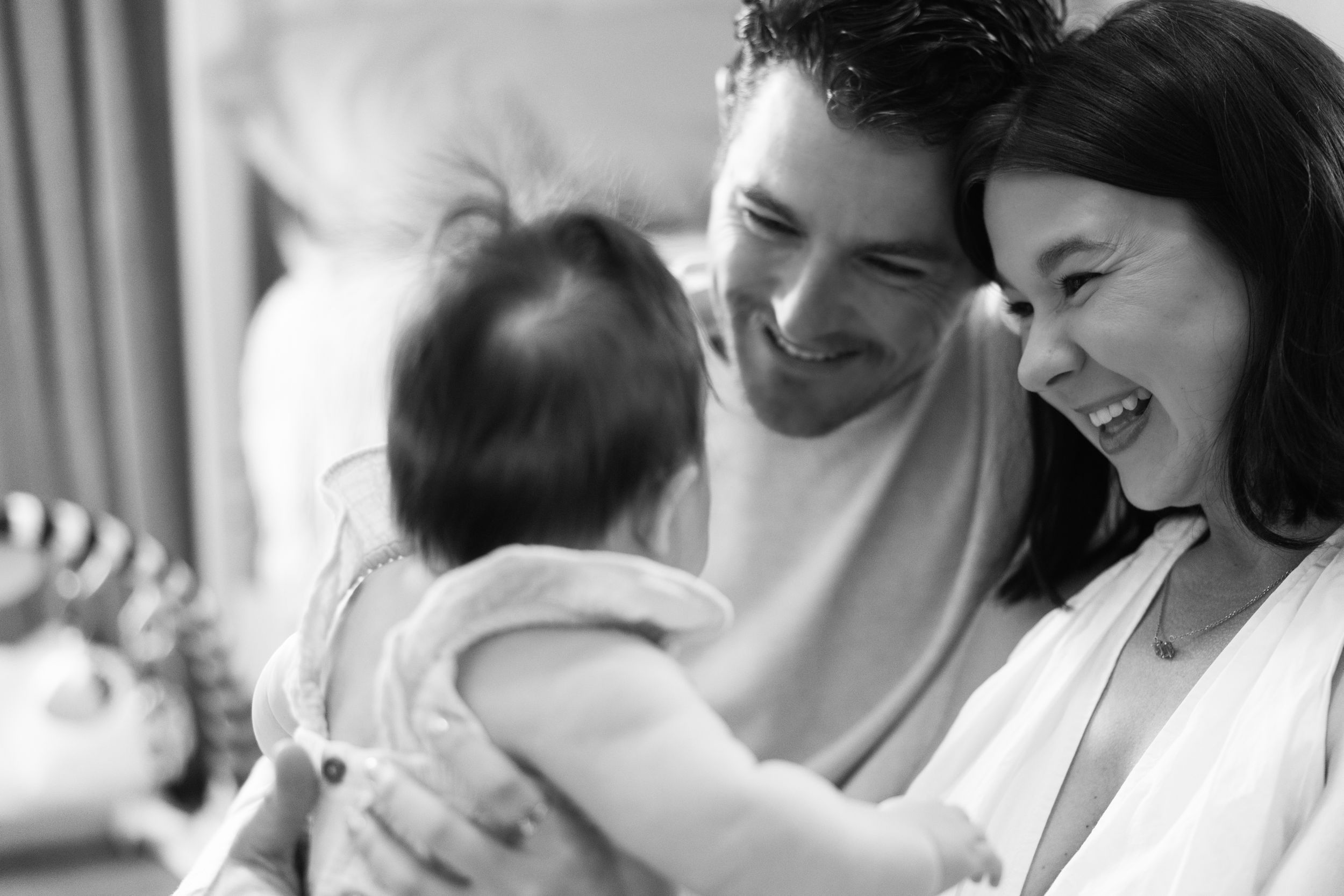 Black and white photo of parents sharing a joyful moment with their baby in a candid family scene.