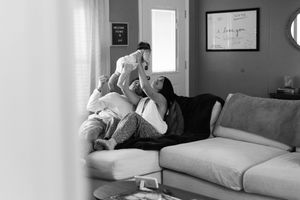 Family sharing tender moment together while relaxing on gray couch in sunlit living room.