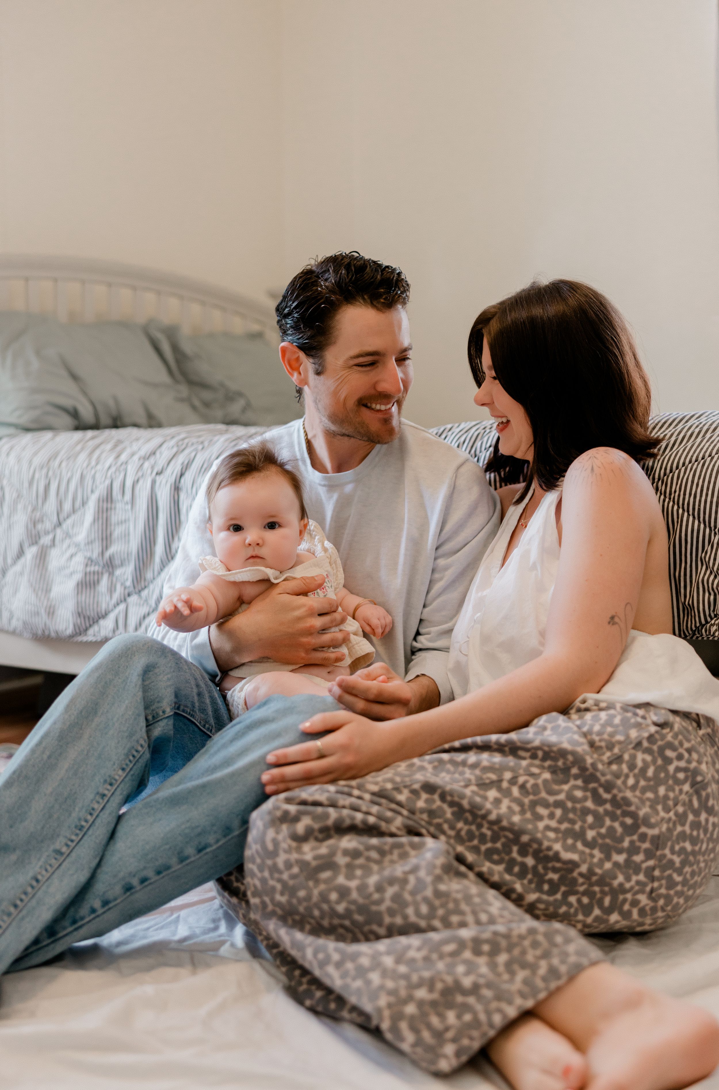 A family shares tender moments while relaxing together on a bed with white linens and a floral print blanket.