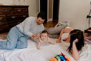 A parent and baby lying on a bed playing with colorful toys and books together.