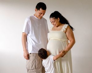 A maternity photo series showing a couple in white clothing against a neutral background during a pregnancy photoshoot.
