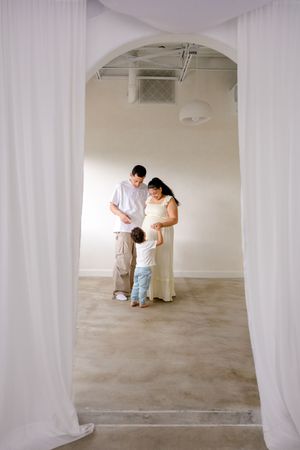 Two people painting a white interior room with arched doorways and bare concrete floors.