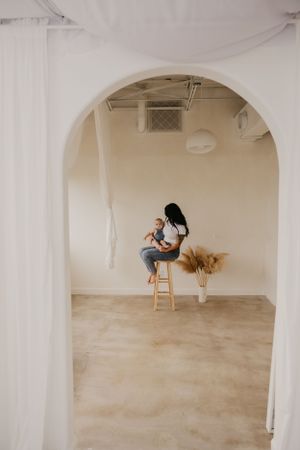 A person sits on a wooden stool in a minimalist white room with pampas grass decor.
