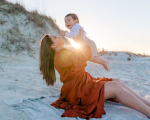 A joyful moment between parent and child playing on sandy beach dunes during sunset.