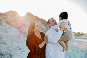 A family shares a joyful moment together on a sun-lit beach with white cliffs in the background at sunset.
