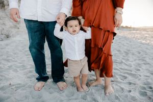 A small child holding hands with adults while standing barefoot on a sandy beach.