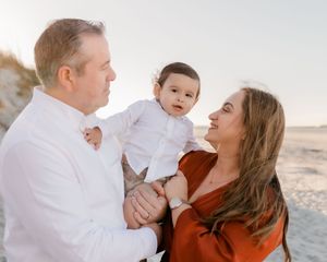 A family wearing white and rust-colored clothing shares joyful moments together on a sunny beach.