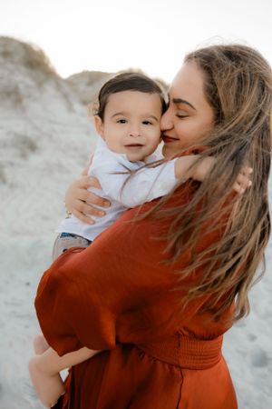 A loving embrace between parent and child set against a pale background, with the parent wearing a warm rust-colored sweater.