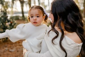 A small child in a white sweater being held and comforted outdoors during a golden-hour photoshoot.