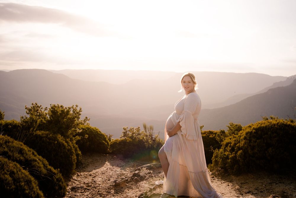 beautiful expecting mother walking along mountain ridge during golden hour.
