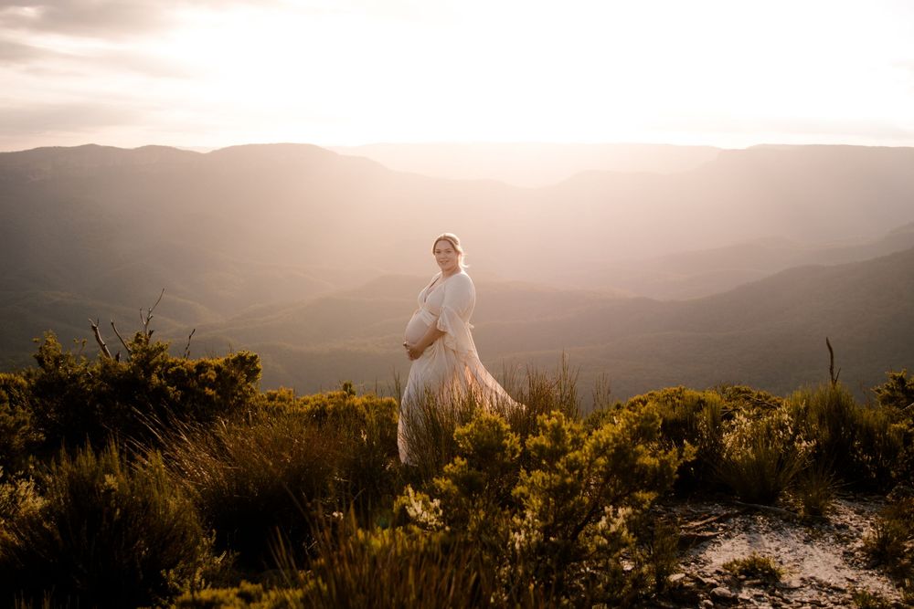 stunning pregnant mama in white dress standing on mountain overlook at sunset.