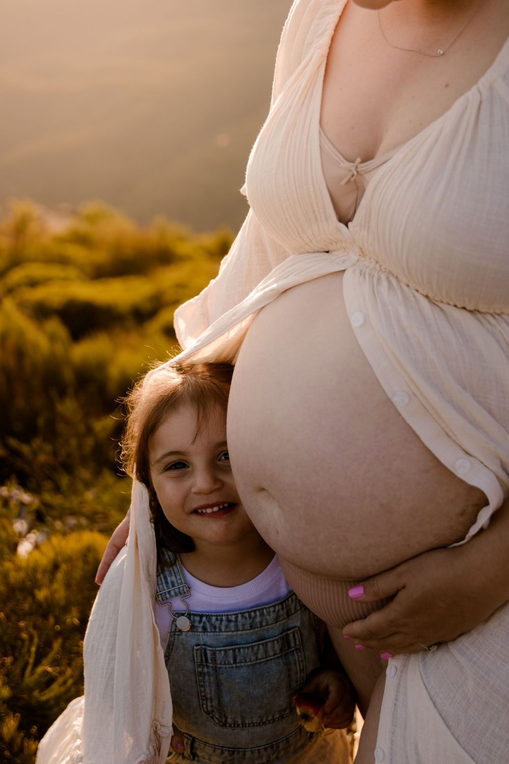 Intimate maternity photo showing pregnant belly and small child in natural sunset lighting.
