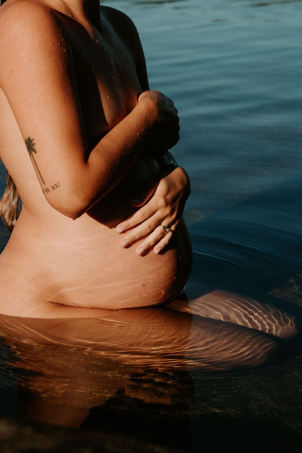 Expecting mother sitting in the ocean at North Curl Curl Beach, hands on her bump, photographed in serene natural light