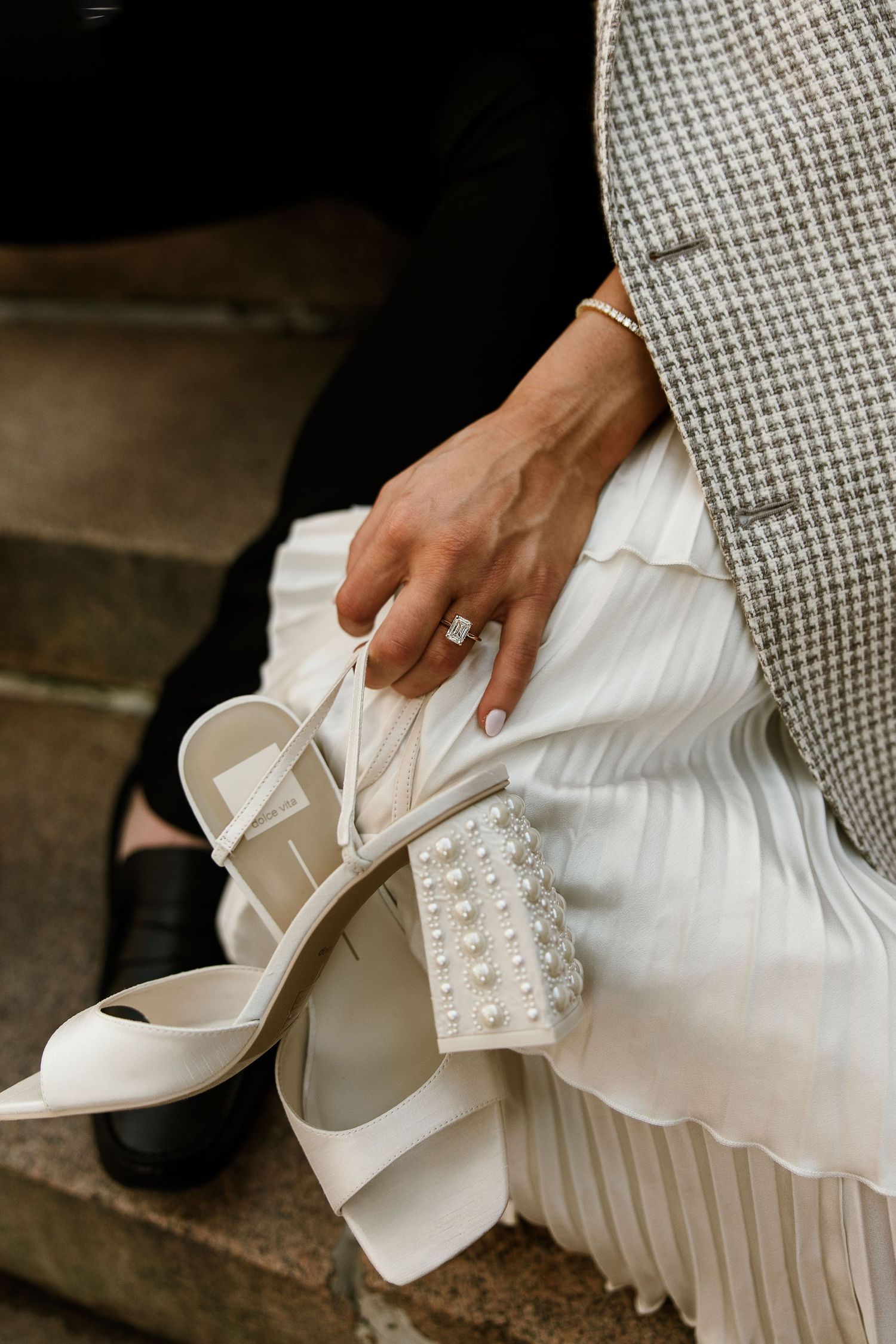 Close-up of bride holding pearl-embellished white heels with diamond engagement ring visible. Providence RI. Miranda Photo & Co
