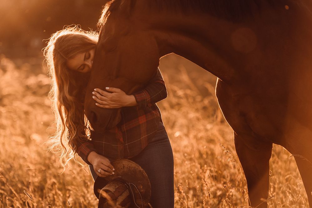 Blonde Frau hält Cowboyhut und küsst ihr braunes Pferd auf die Nase