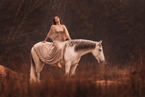 Dunkelhaarige Frau im Shootingkleid auf weißem Pferd