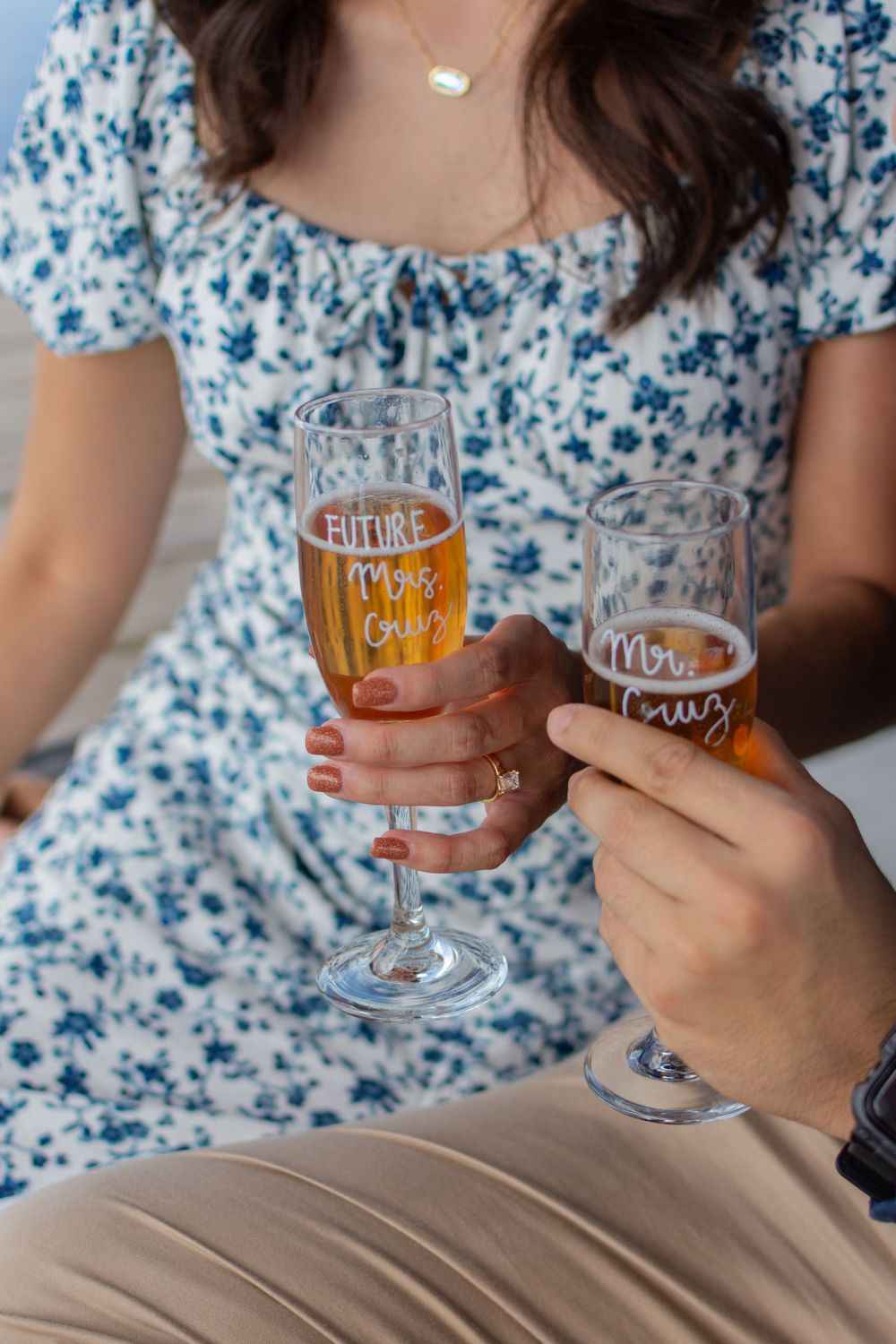 Close-up of champagne flute glasses in a couples' hands that say Future Mrs. Cruz and Mr. Cruz, made by the woman's friend. Her ring shows.