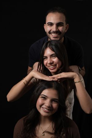 Three smiling young people posing together against a dark background in a stacked portrait arrangement.
