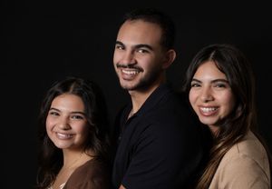 Three young adults smiling together against a dark background in a professional portrait photo.