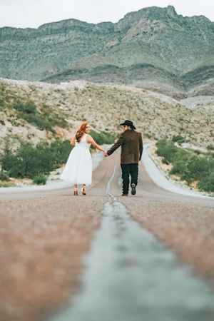 Newlywed couple walking hand in hand on a desert mountain road.