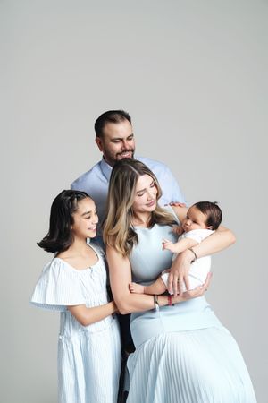 A happy family of four with a newborn baby poses together in coordinating blue outfits.