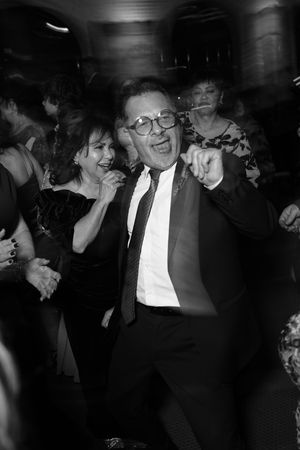 Man in suit and glasses dancing joyfully at a lively black and white party event.