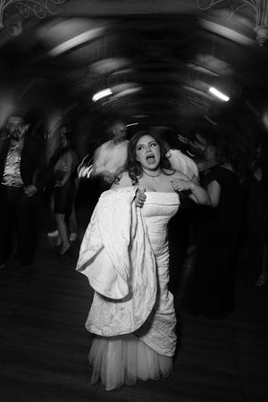 Bride in white lace wedding dress dancing energetically at reception in black and white photo.