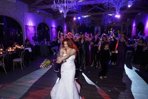 Bride and groom share a romantic dance on the floor at an elegant purple-lit wedding reception venue.