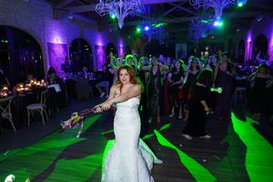 Bride in white gown tosses bouquet under green lights at elegant wedding reception.