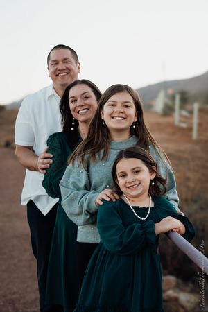 A smiling family of four poses outdoors in coordinating green and white outfits during a professional portrait session.