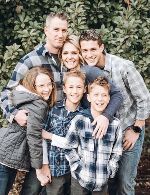 Family group wearing plaid shirts and casual clothing pose together against green foliage background.