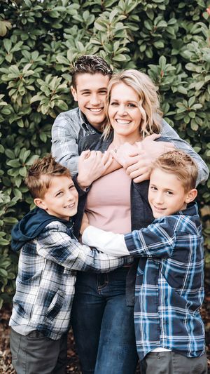 Family wearing coordinating plaid shirts embrace in casual portrait against leafy background.