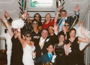 Wedding guests wave and celebrate in a panoramic group photo during a joyous reception moment.