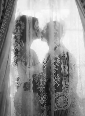 Silhouettes of two figures embracing behind romantic lace curtains in a dreamy black and white vintage photograph.