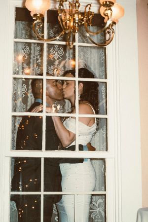 Romantic scene through window panes with delicate lace curtains and warm chandelier lighting at dusk.