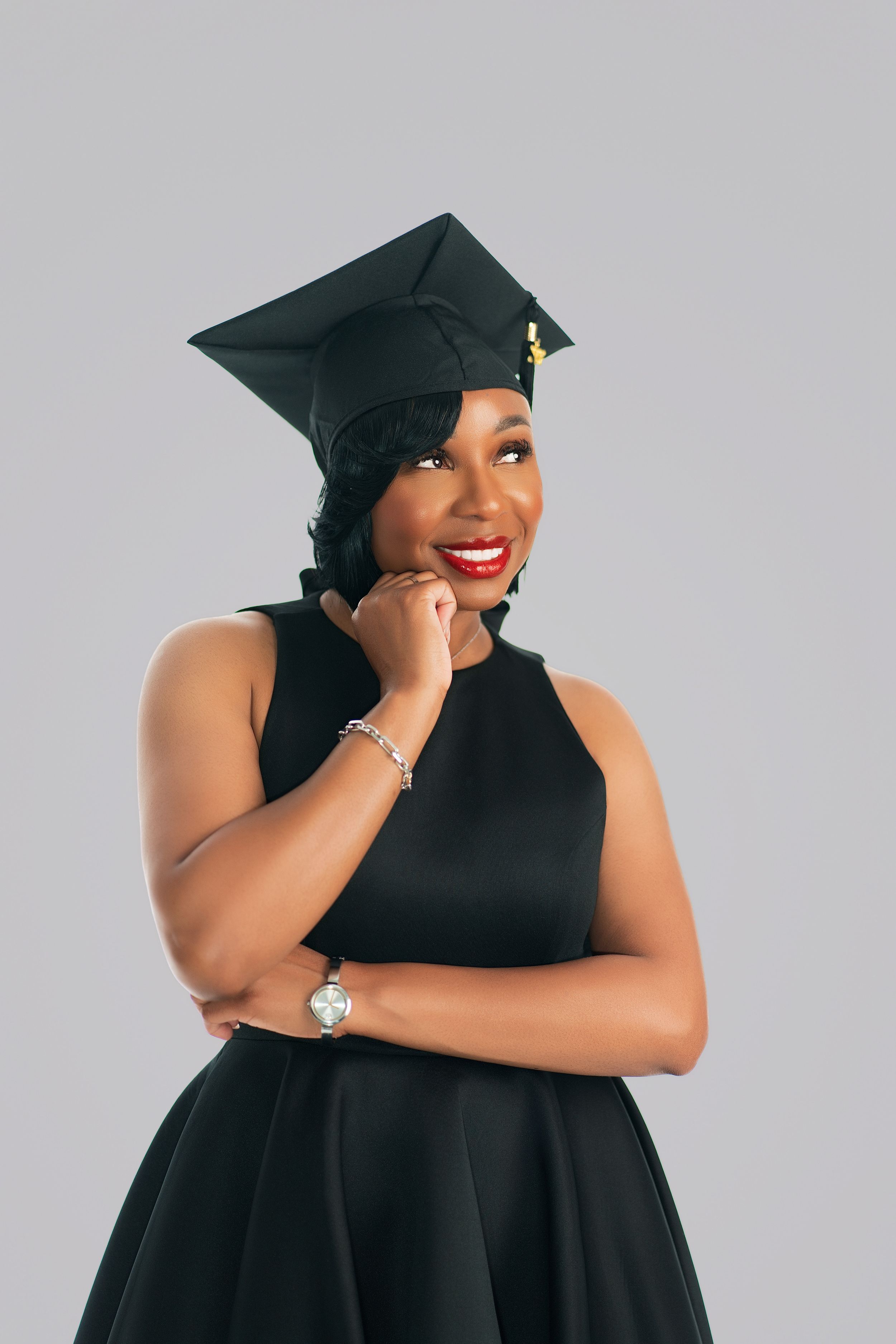 Smiling woman in black graduation cap and dress posing confidently against a gray background.